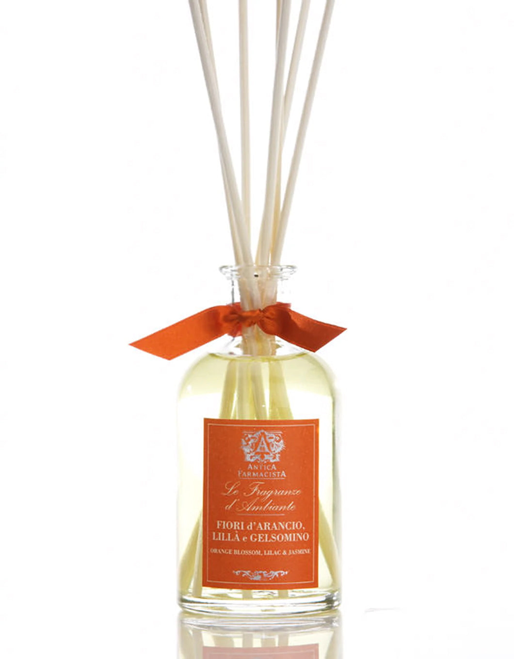 Domed glass container with white reeds orange Antica Farmacista label orange satin ribbon tied around neck of bottle.